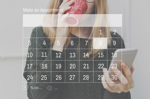 Woman drinking from cup whilst looking at screen with appointment calendar